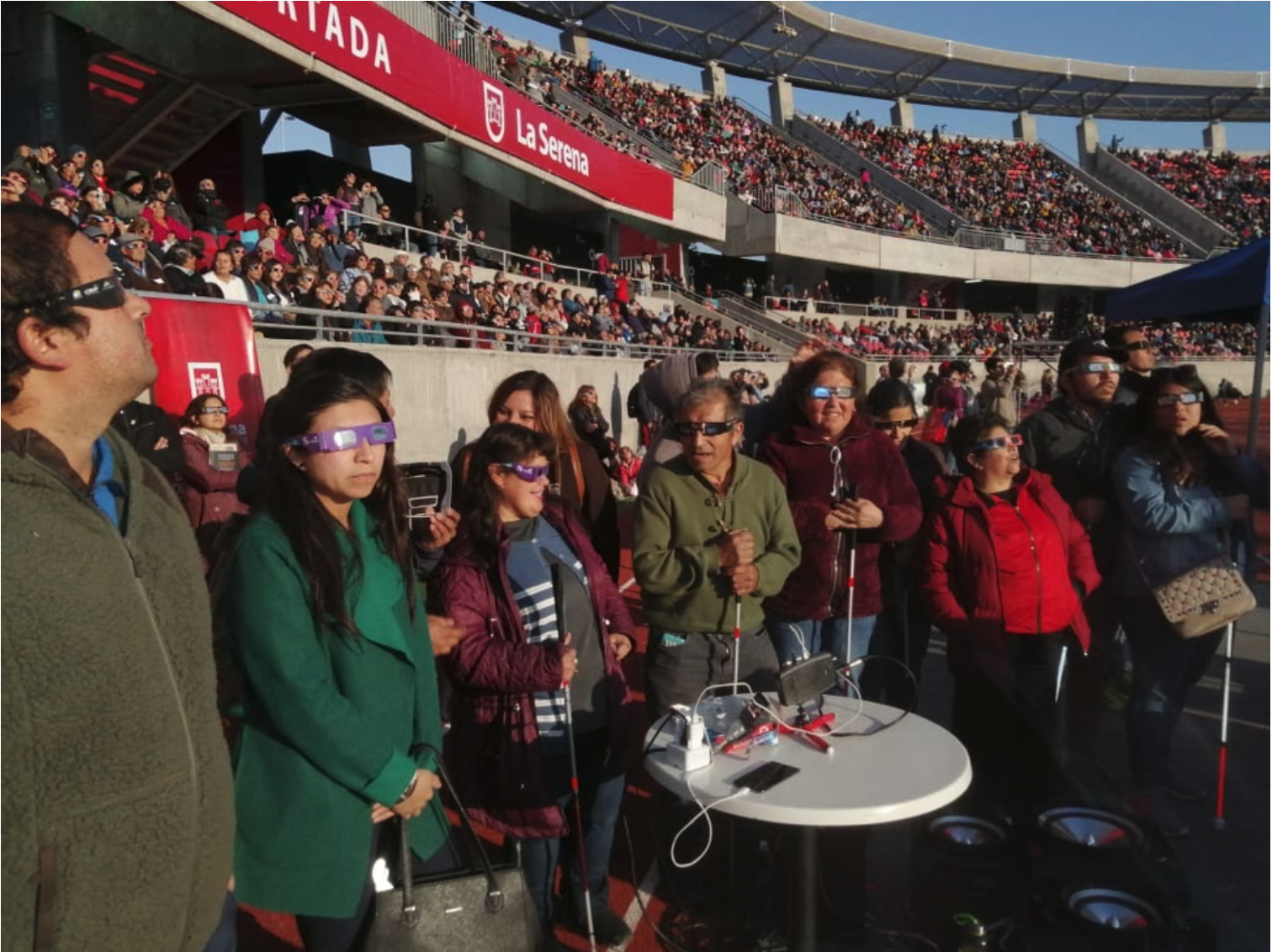 Thousands of people gathered at La Portada Stadium in La Serena, Chile during the 2 July 2019 solar eclipse. A LightSound device is positioned on a table and connected to a large speaker to project the sound to the crowd.